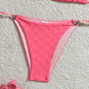 Detail view of pink checkered bikini bottom with faux pearl straps on plush white background
