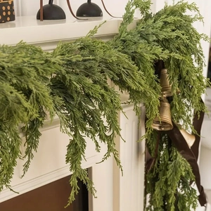 Artificial cypress garland with bronze bells and brown ribbon on a white fireplace mantel