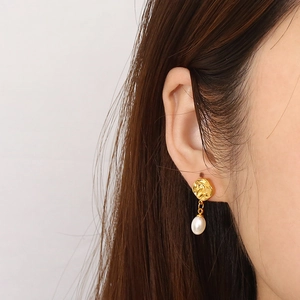 Gros plan d'une boucle d'oreille dorée à texture irrégulière avec pendentif perle blanche
