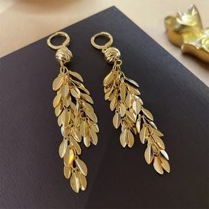 Detailed view of golden leaf tassel earrings on dark wood surface with sequins