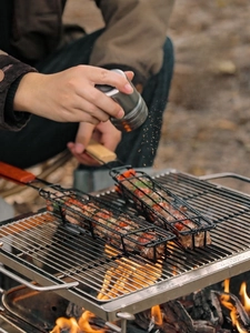 Outdoor BBQ cage with wooden handle for grilling meat and vegetables during camping