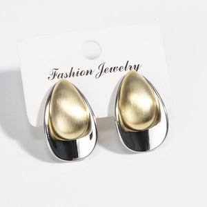 Macro detail of tear-drop earrings featuring brushed gold and polished silver finish