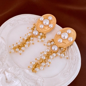 Detailed close-up of vintage gold tassel earrings with oval pearls on decorative tray