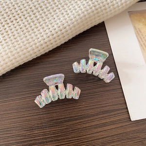 Detailed view of iridescent mini hair claws with wave design on rustic wood background