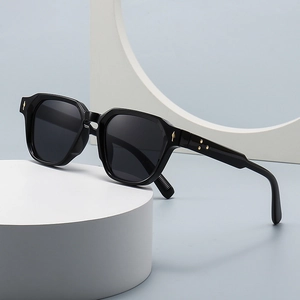 Retro black narrow frame sunglasses with gold metal accents on white geometric props