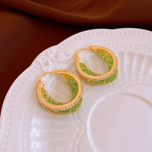 Close-up of golden leaf-inspired hoop earrings with green mesh and sparkling crystals