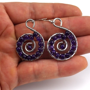 Detail of handmade wire wrapped purple bead spiral earrings held in hand for scale