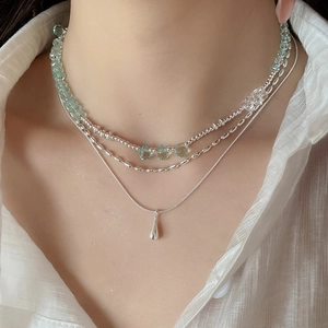 Close-up of triple-layered silver necklace with light green beads and waterdrop pendant
