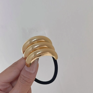 Detailansicht eines schwarzen Haargummis mit drei glänzend goldenen Metallakzenten