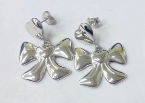 Close-up of silver bow stud earrings with heart detail and high polished finish