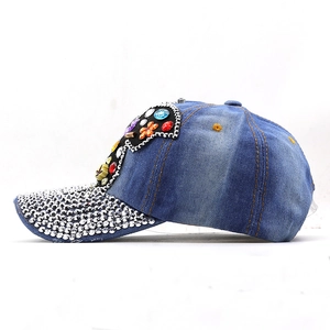 Détail d'une casquette en denim bleu avec motifs floraux en strass colorés et bijoux