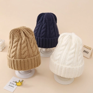 Close-up of cable knit textures on thick winter beanies in camel, navy, and white colors
