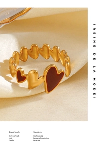 Close-up of 18K gold plated heart ring with red enamel details on silk fabric