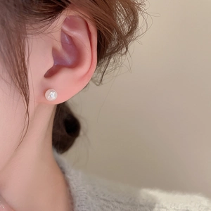 Close-up of minimalist white pearl stud earrings worn by a model in soft warm lighting