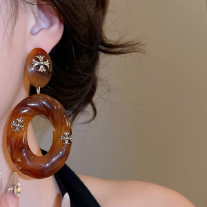 Detail of acrylic tortoiseshell hoop earrings featuring silver gothic cross embellishments