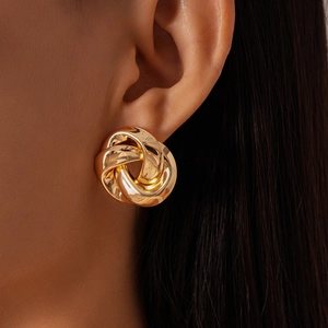Detailed view of a gold-toned twisted knot stud earring worn on a model's earlobe
