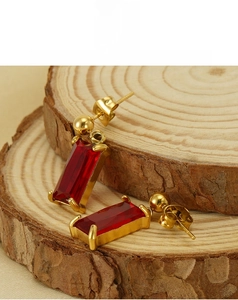 Detail view of rectangular red zircon earrings with gold plating on a natural wood surface