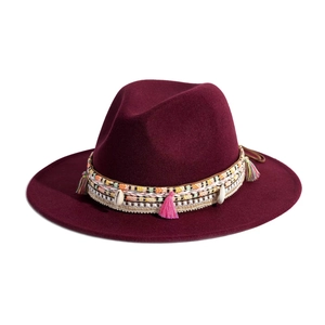 Detail of burgundy wide brim fedora hat with bohemian tassel and shell decorative band