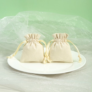 Close-up of beige cotton linen drawstring jewelry pouches on a white ceramic plate