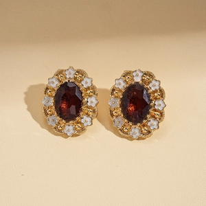 Detail of vintage gold flower earrings with oval dark red gemstone and white petals