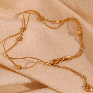 Detail view of double-layer gold snake chain anklet with cube beads on silk background