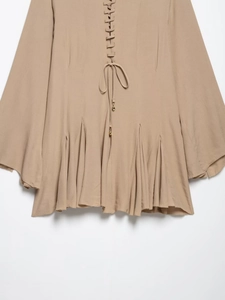 Detail of khaki chiffon dress featuring bell sleeves and tie-front with metal charms