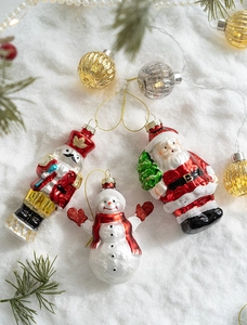 Close-up of glass Santa, snowman and nutcracker ornaments on snow with pine and warm lights