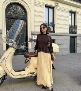 Détail d'une jupe longue plissée jaune pâle avec un haut marron à manches longues et volants