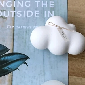 Vela artesanal con forma de nube en mesa de madera con etiquetas de papel mínimas