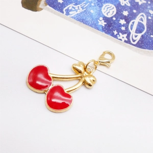 Close-up of a red enamel cherry charm with golden metal finish and lobster clasp detail