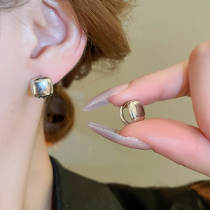 Detailed view of silver square hoop earrings on ear and hand with metallic finish