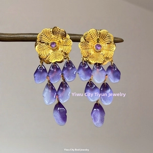 Détail de boucles d'oreilles pendantes avec fleurs dorées et pétales violets sur bois