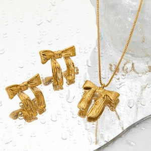 Golden textured bow necklace and earrings set displayed on a reflective mirror surface