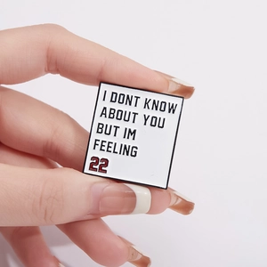 White square metal enamel pin featuring Taylor Swift 22 lyrics and red number detail