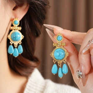 Close-up of vintage golden drop earrings with turquoise stones and resin teardrop pendants
