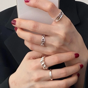 Detail of silver knot and chain link rings set on female hand with black suit background