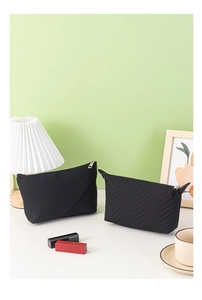 Detail of two black dumpling cosmetic bags with V-shaped quilting on a modern desk