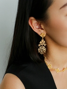 Close-up of golden vintage hollow floral earrings and matching clover necklace on model
