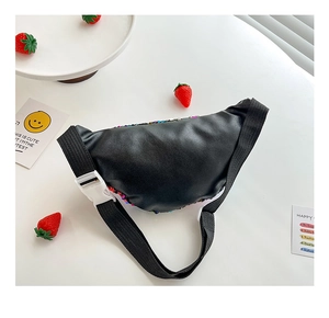 Top-down view of black sequined children's waist bag on a white desk with decor