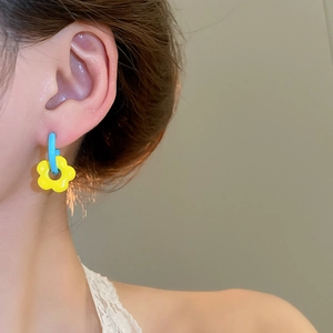 Detail shot of a model wearing yellow floral earrings with light blue enamel hoops