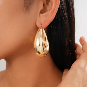 Close-up of a large gold teardrop earring featuring a high-polish metallic mirror finish