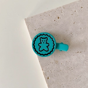 Detailed close-up of blue metal hair clip with cute bear pattern on marble surface