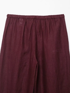Detail of burgundy linen trousers featuring a textured elastic high waist and breathable fabric