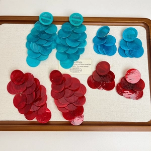 Detail of layered round sequin drop earrings in blue and red on a wooden jewelry tray