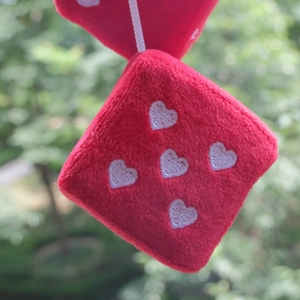 Detail of red plush car dice with white embroidered heart patterns and hanging rope