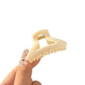 Mini cream butterfly hair claw clip with pointed teeth shown in a handheld close-up view