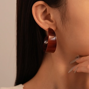 Detail of amber acrylic C-shaped hoop earring worn by a model in soft lighting