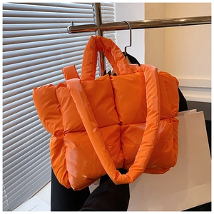Detail of bright orange puffer tote bag showing glossy quilted fabric and padded handles