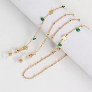 Detail of golden glasses chain with green beads and heart charms on white display