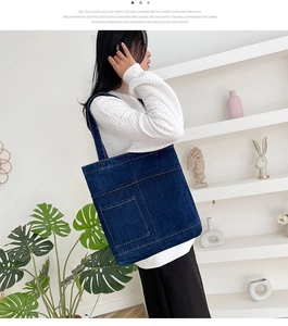 Dettaglio di una grande borsa tote in denim blu navy con cuciture a vista sulla tasca frontale